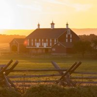 A picturesque red barn surrounded by greenery under a sunset sky.