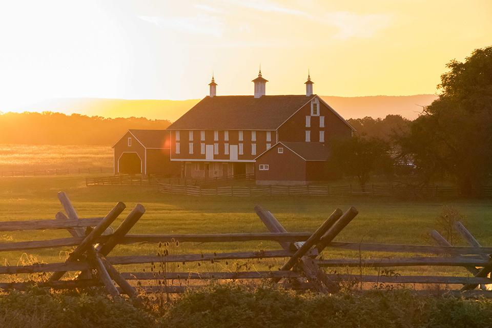 A picturesque red barn surrounded by greenery under a sunset sky.